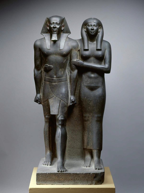 <ul><li><p><u><strong>Form</strong></u></p><ul><li><p>Two figures attached to a block of stone; arms and legs not cut free.</p></li><li><p>Traces of red paint exist on Menkaura’s face and black paint on the queen’s wig.</p></li><li><p>Figures seem to stride forward, but simultaneously are anchored to the stone behind; it is unusual for the female figure to be striding with the male. The female is similar in size, indicating equality.</p></li><li><p>Menkaura’s powerful physique and stride symbolize his kingship, as does his garb: nemes on the head, an artificial beard, and a kilt with a tab.</p></li></ul></li><li><p><strong>Function</strong></p><ul><li><p>Receptacle for the ka of the pharaoh and his queen.</p><ul><li><p><strong>Ka</strong>: the soul, or spiritual essence, of a human being that either ascends to heaven or can live in an Egyptian statue of itself</p></li></ul></li><li><p>Wife’s simple and affectionate gesture, and/or presenting him to the gods.</p></li></ul></li><li><p><u><strong>Materials</strong></u>: Extremely hard stone used; symbolizes the permanence of the pharaoh’s presence and his strength on earth..</p></li></ul>