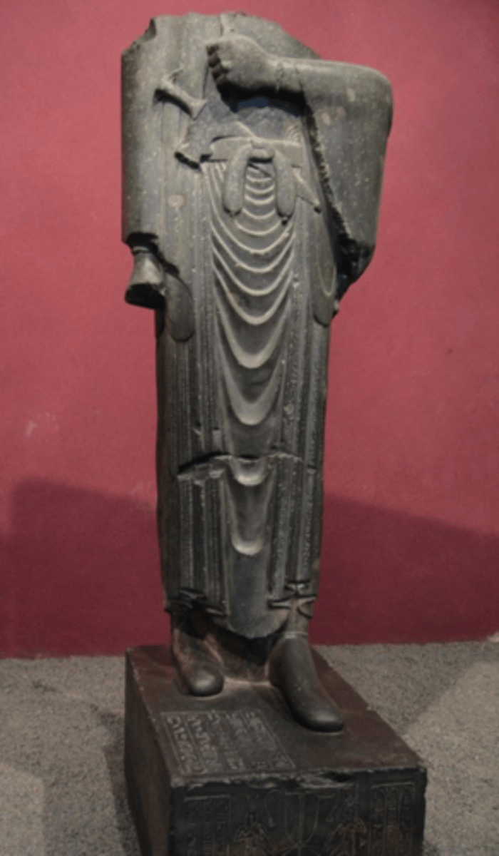 <p>Placed in Egypt. Wearing a dress, and a sword decorated with jewels on his belt.</p><p>Only freestanding statue in ancient Persia.</p><p>On the sash of the belt of the statue of king Darius the Great are signs in hieroglyphic script that spell his pharaonic name - cultural tolerance.</p><p>Although the statue is in a clear Egyptian nature, Darius also carries a lotus flower and a staff in his hands, common Persian symbols of authority - sinister undertone.</p><p>A pharaoh would've carried other attributes - his robe is also Iranian.</p>