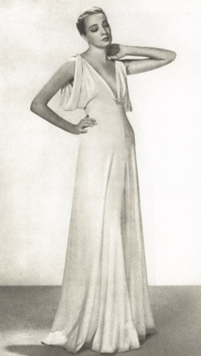 <p>a draped, figure-hugging silhouette that flows and flares at the hem</p>