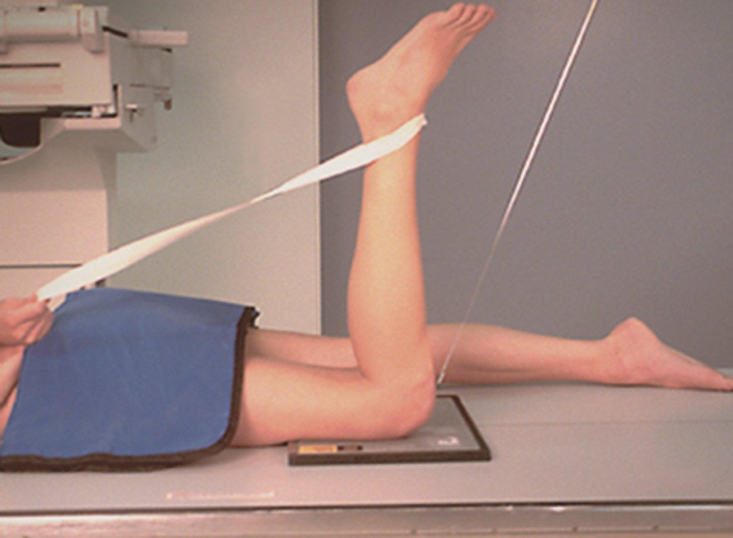 <p>▪ Patient lies prone.</p><p>▪ The IR can either be directly under the knee or in this case within the bucky (not using grid/AEC)</p><p>▪ Knee is flexed through 90 degrees.</p>