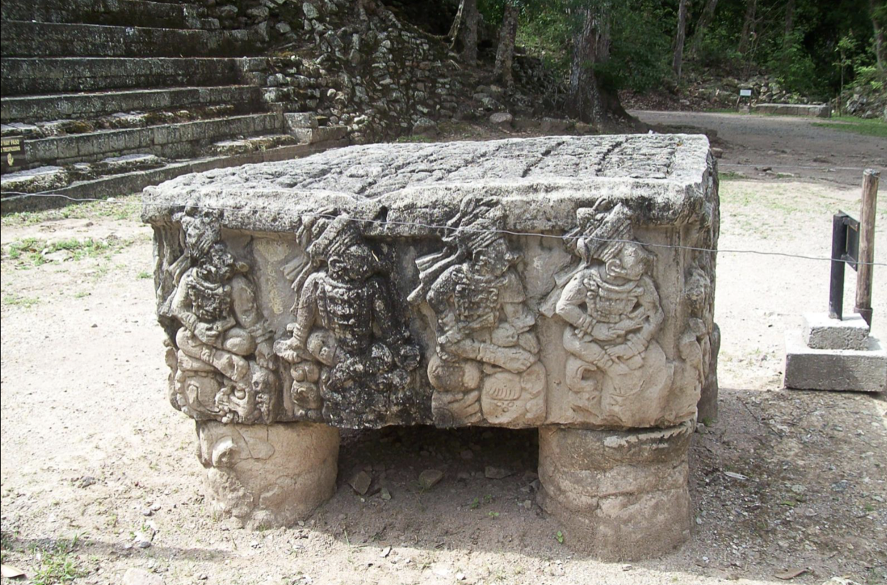 <p>almost looks like a raised platform or table. located in front of pyramid, glyphic inscription on top. rulers of the late classic dynasty on the sides, starting with founder yax-kuk-mo. 16 rulers total. appears that yax-kuk-mo is giving the bisophalic rod to the most recent ruler, yax-pac. seated in a circle meaning everything around them is within the circle because they face outward - we are within their circle.</p>