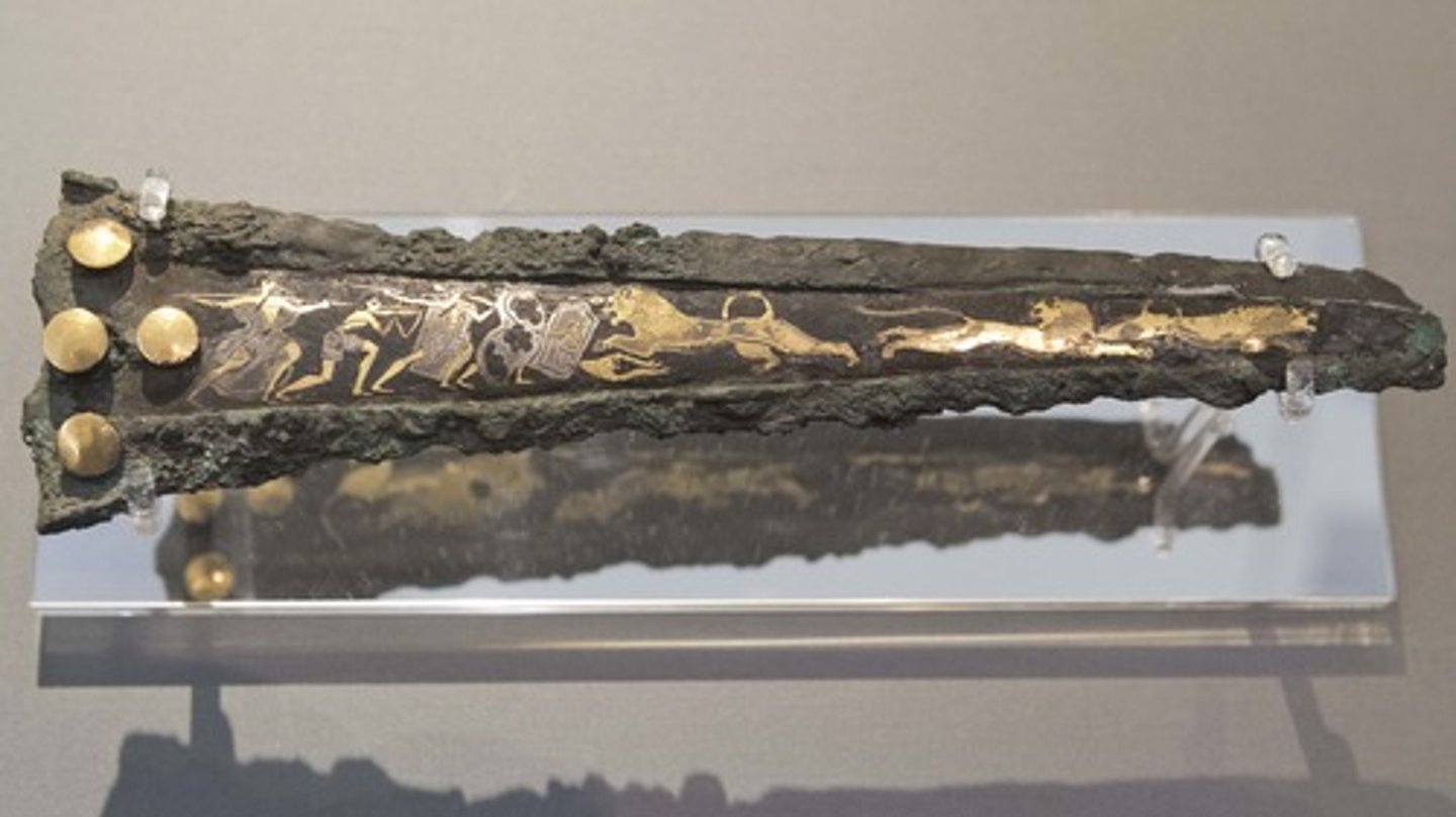 <p>Who:</p><p>The artist is unknown, but it's attributed to the Mycenaean civilization12.</p><p>What:</p><p>This is a dagger made of bronze, with gold, silver, and niello inlay1. The scene on the dagger blade shows male hunters carrying large shields, semi-cylindrical or figure-of-eight shaped1.</p><p>Where:</p><p>The dagger is currently housed in the National Archaeological Museum of Athens3.</p><p>Original Findspot:</p><p>The dagger was found in Shaft Grave IV in Grave Circle A at Mycenae12.</p><p>When:</p><p>The dagger dates to around 1725-1600 BC12.</p><p>Why it's interesting and important:</p><p>The Niello dagger from Shaft Grave IV is one of the most famous artifacts from Mycenae. It provides valuable insights into Mycenaean warfare and their advanced metalworking techniques2. The scene on the dagger blade is a testament to the Mycenaean's martial culture and their use of large shields for protection1.</p>