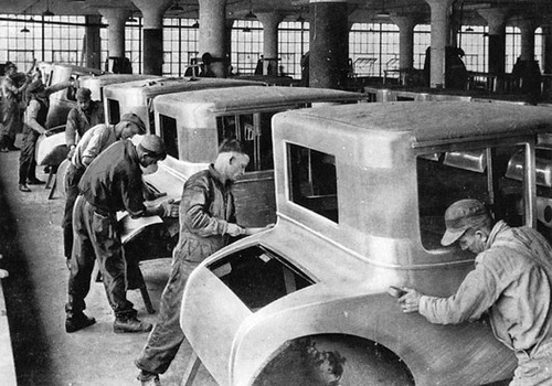 method of production in which workers stay in one place as products edge along a moving belt