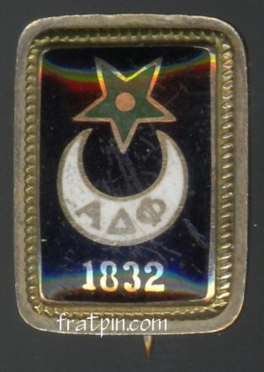 <p>oblong slab with rounded corners, displaying on a shield of black enamel a white crescent bearing the letters alpha delta phi. above the crescent, a UPSIDE DOWN green star with a gold center, and below the date 1832 in gold. on the back SWORD AND SPEAR BOTH POINT LEFT</p>