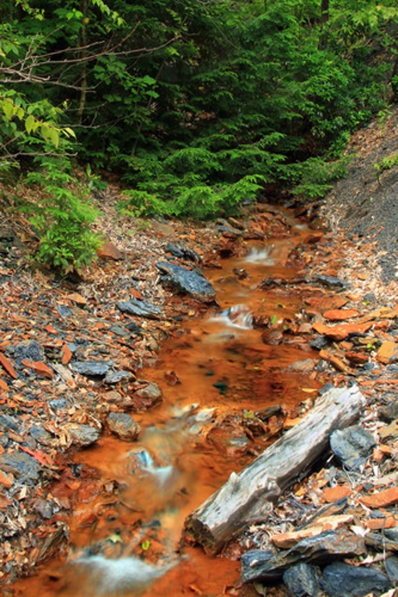 <p>Acidic water formed when mine waste reacts with air and water, polluting streams.</p>