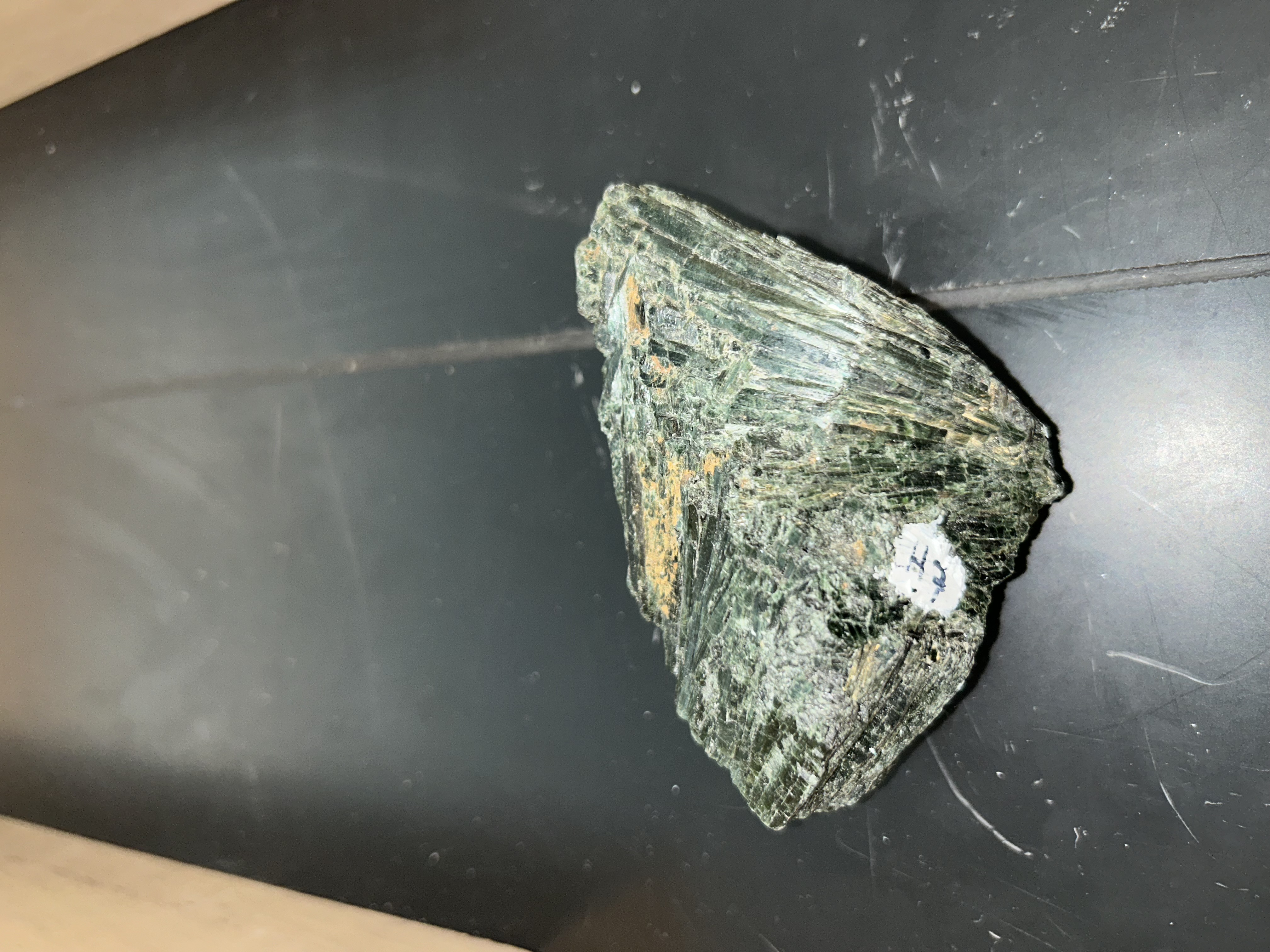 <p>dark green color </p><p>larger elongated fibrous crystals </p>