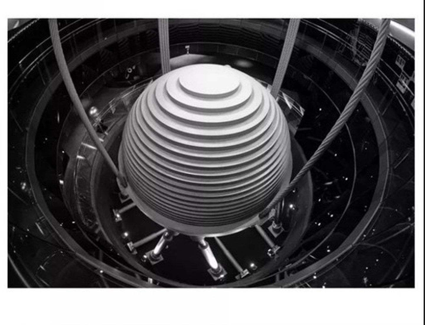 <p>a heavy mass mounted on rollers or suspended with cables and attached to the upper portion of a tall building with spring damping mechanisms, having an inertial tendency to remain at rest and thus counteracting and dissipating any building movements</p>