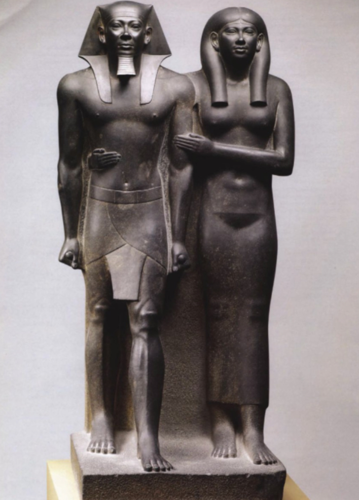 <ul><li><p>From Giza, Egypt</p></li><li><p>Made out of Greywacke (a hard, volcanic stone)</p></li><li><p>ca. 2475 BCE (Old Kingdom)</p></li><li><p>Shows King Menkaure and his queen/queen mother. King is very rigid in pose, actually idealized version. Wears king’s nemes head covering, fake beard, a kilt (made for spirits in afterlife) and wide belt.</p></li><li><p>Queen is slightly smaller, holds king’s arm and her arm encircles his waist. Has a wig over natural hair (line in the middle shows this) & wears a sheer gown. Face is rounded and “youthful”</p></li><li><p>Head covering and wig shows only superiors can only wear them.</p></li></ul>