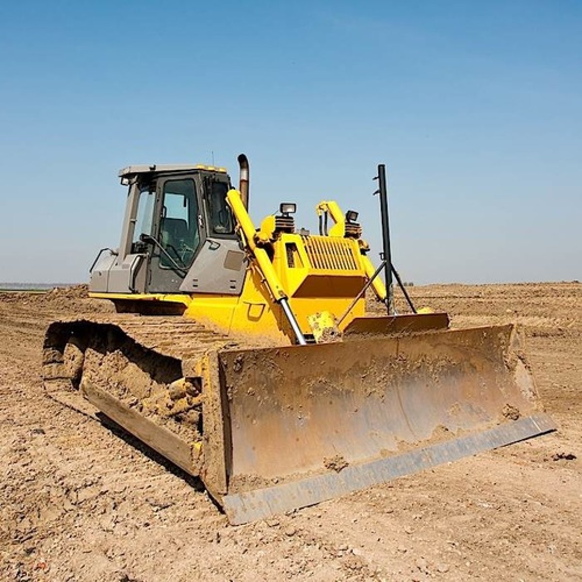 <p>is a tractor with a pushing blade which moves earth and clears land of bushes and trees</p>
