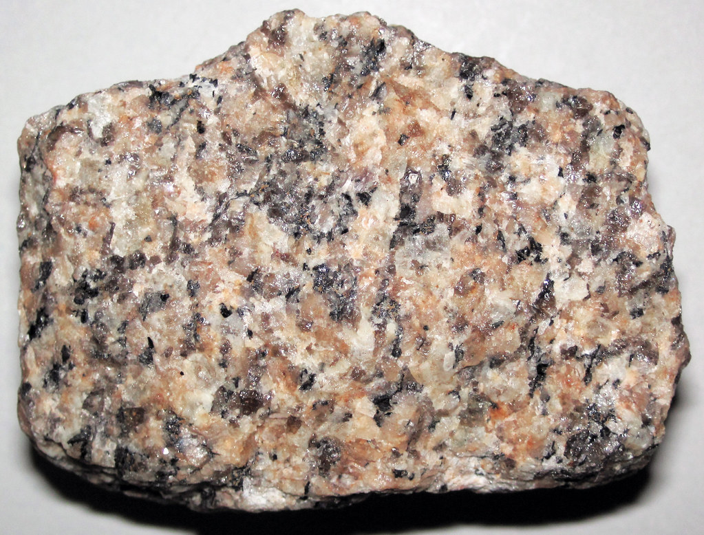 <p>Igneous rock: Granite</p><p><strong>Granite is an intrusive igneous rock composed primarily of feldspar, quartz, and smaller amounts of mica. It has a phaneritic texture, meaning its tightly interlocking crystals can be seen with the naked eye. It usually displays mottled colors of off-white, gray, pink, and black with no layering or banding.</strong></p><p><strong>Granite has a coarse-grained texture with large, interlocking crystals of translucent to off-white quartz, white to dark pink feldspar, and darker micas and amphiboles. Its crystals are roughly equal-sized and it is relatively light in color, lacking any structural features like layering, banding, or fossils.</strong></p>