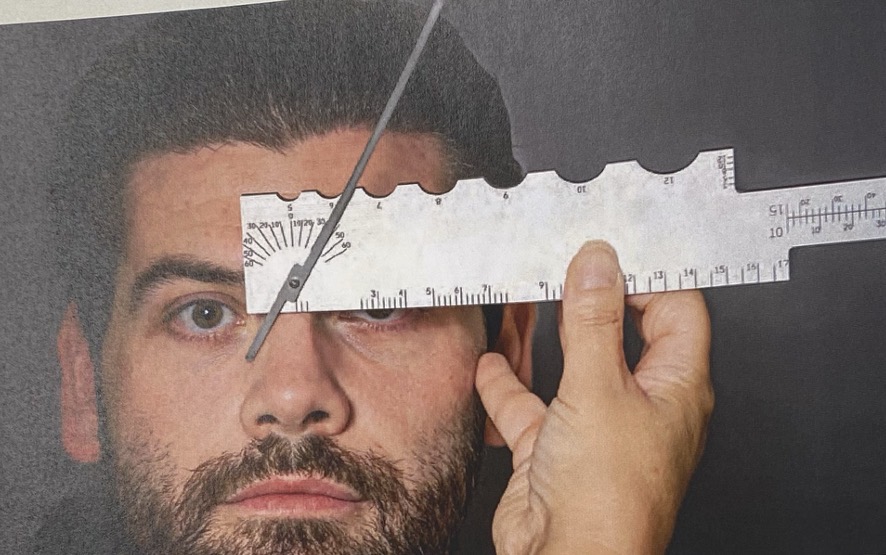 <p>With the hand holding the end of the gauge, rotate the pointer so that it rests along the bearing surface of the nose, where the pad of the frame would rest. The left side of the pointer will indicate the frontal angle on the protractor. Repeat for the other side.</p>