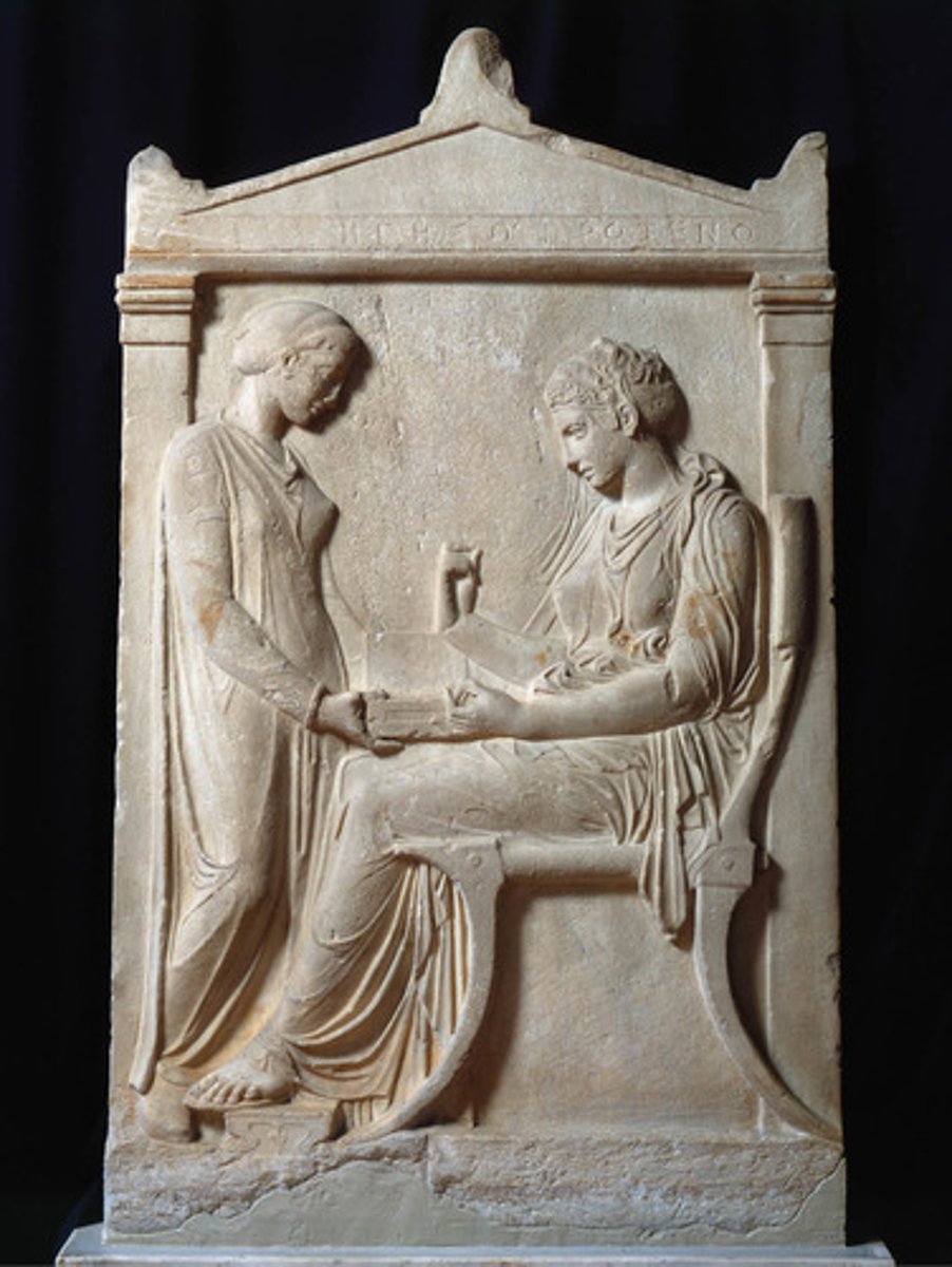 <p>Hegeso's stele; she wears heavily draped and modest clothing and is attended to by a slave as she sits on a chair inside holding a jewellery box, showing her wealth</p>