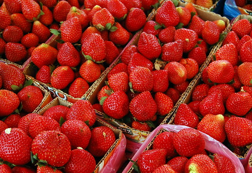 small, triangular shaped red fruits with small seeds all over them. They have white interiors with small green leaves and green crowns.