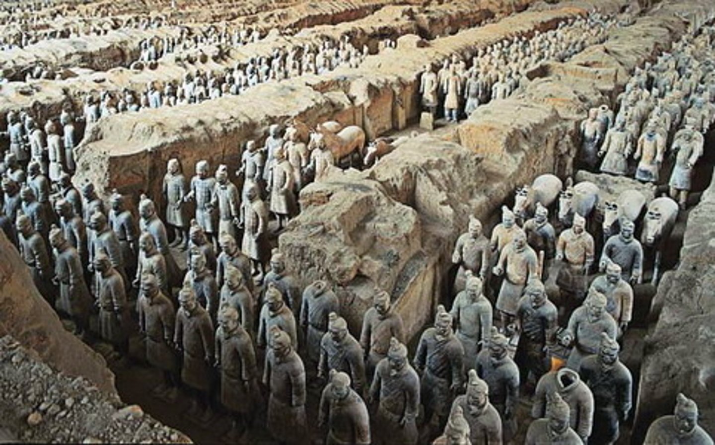 <p>- An army of over 8,000 life-sized clay soldiers buried with Emperor Qin Shi Huang (d. 210 BCE)</p><p>- Each figure is unique, with individual faces, hairstyles, and rank-specific details</p><p>- Arranged in military formation in underground pits near the emperor's tomb at Xi'an</p><p>- Originally painted in bright colors, now faded after exposure to air</p><p>- Discovered in 1974 by farmers digging a well — one of the greatest archaeological finds of the 20th century</p>