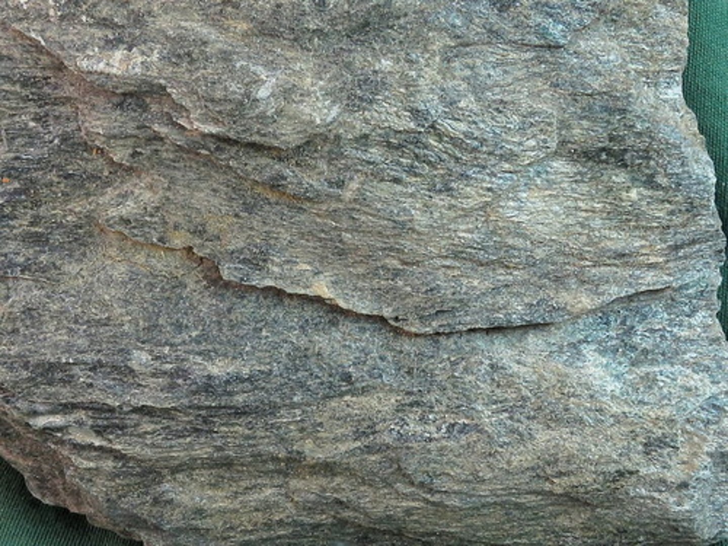 <p>A fine-grained, well-foliated rock in which the grains are barely visible with a hand lens as shiny flakes. Sheet silicates are abundant (typically muscovite and chlorite), and quartz veins may be visible. Although individual crystals are generally too small to identify, the overall effect of grain size and foliation gives the rock a satin-like reflectivity.</p>