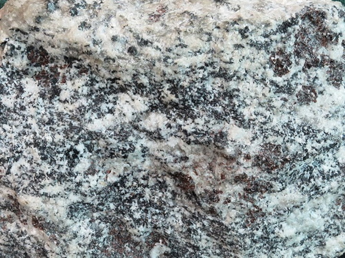 <p>A medium- to coarse-grained, generally mica-poor rock having poor foliation. Minerals are easily visible and identifiable by eye or with a hand lens or microscope. The dominant minerals are feldspars and quartz. This one also contains black biotite and dark-red garnets.</p>