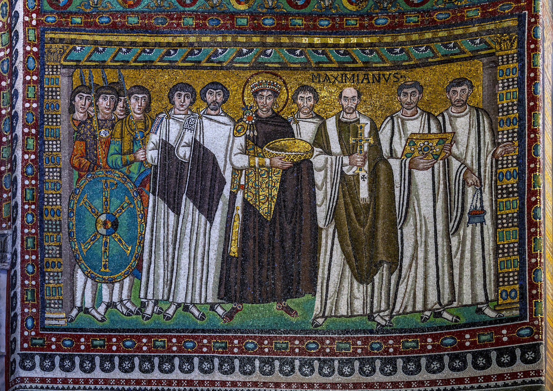 <p>-c. 547 C.E. Ravenna, Italy</p><ul><li><p>the main theme is the authority of the emperor in the Christian plan of history</p></li><li><p>Justinian is frontal in the center of the mosaic; he wears a purple robe and a crown, surrounded by members of the clergy</p></li><li><p>The left figure is the Bishop Maximianus of Ravenna, and the right is members of the imperial administration with purple stripes on their robes trailed by soldiers</p></li><li><p>they carry a censer, the gospel book, the cross, and the bowl for the bread of the Eucharist. _Justinian&apos;s Mosaic sits adjacent to the mosaic of Christ, who is also dressed in a purple robe. _Justinian overlaps standing with the pope making him the closest to the viewer</p></li></ul>