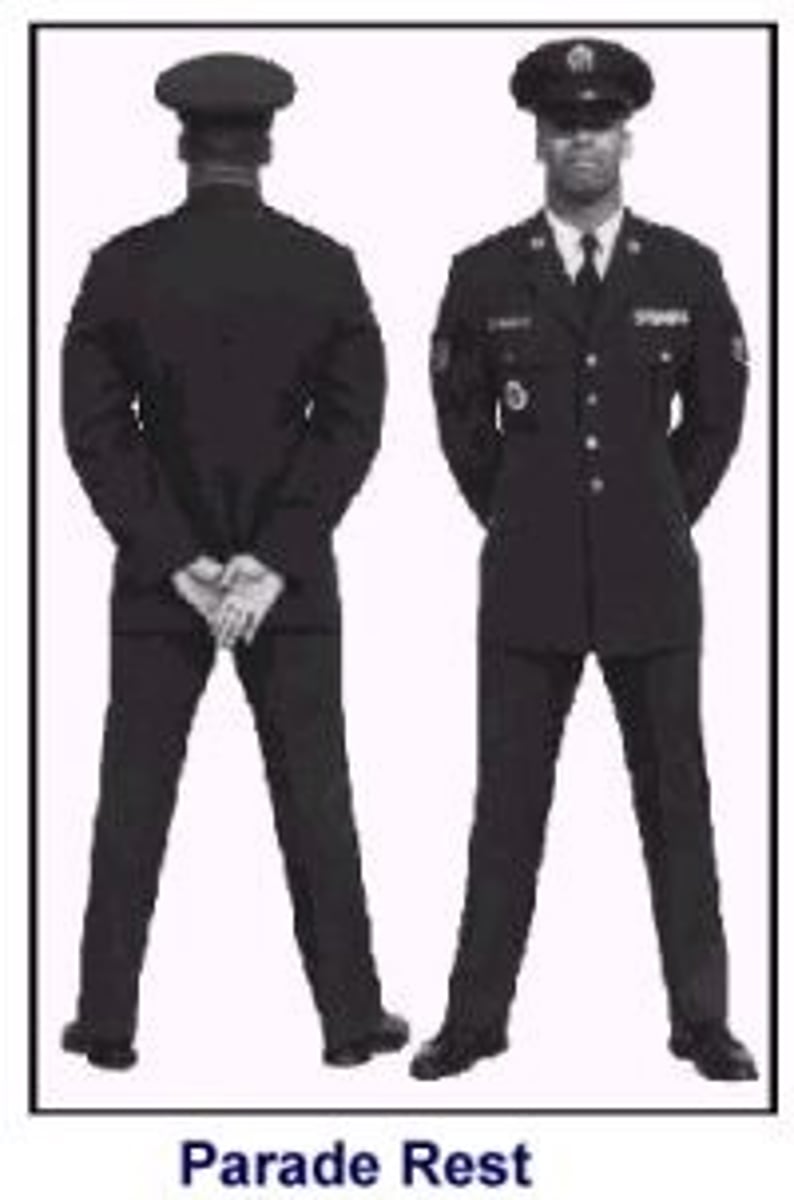 <p>The command is PARADE, REST. On the command REST, the airman will raise the left foot from the hip just enough to clear the ground and move it smartly to the left so the heels are 12 inches apart, as measured from the inside of the heels. Keep the legs straight, but not stiff, and the heels on line. As the left foot moves, bring the arms, fully extended, to the back of the body, uncapping the hands in the process; and extend and join the fingers, pointing them toward the ground. The palms will face outwards. Place the right hand inthe palm of the left, right thumb over theleft to form an "X" (figure 2). Keep head and eyes straight ahead and remain silent and immobile.</p><p>https://www.youtube.com/watch?v=onGybrxXSIs</p><p>0:00-0:54</p>